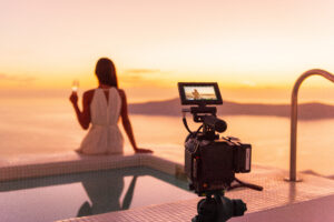 woman with glass of wine watches sunset by the pool with camera set up behind her