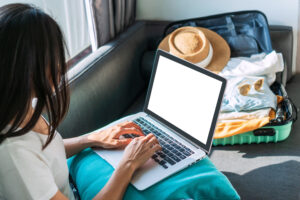 woman on laptop with open, packed suitcase beside her