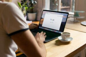 person using a laptop with the Google search page visible and an empty coffee cup beside them