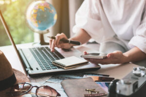 traveller planning trip at laptop surrounded by travel paraphernalia 