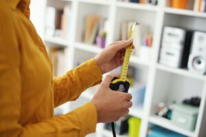 woman's hands holding a measuring tape in front of shelves